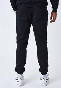 Pantalones de chándal negros con puños elásticos, bolsillos laterales y una textura suave, combinados con zapatillas Nike blancas que tienen un logotipo negro.