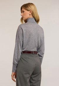 Šedý svetr s rolákem a dlouhými rukávy, spárovaný se šedými pruhovanými kalhotami a bordó opaskem s krokodýlími vzory.