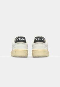 Sneaker bianche in pelle con suola in gomma crema. Presentano una linguetta nera sul tallone con il logo "VEJA" e accenti grigi. Design minimalista.