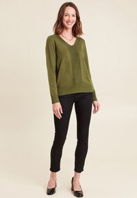 Olijfgroene v-hals trui met een gestructureerd verticaal paneel, gecombineerd met zwarte slim-fit broek en zwarte hoge hakken.