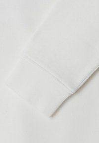 Tela de sudadera blanca que muestra un primer plano del puño, con una textura acanalada y detalles de costura pulidos. Material suave y liso.