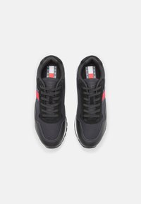 Sneakers atletici neri realizzati in tessuto e suede, con una striscia rossa, lacci tondi e suola in gomma testurizzata.