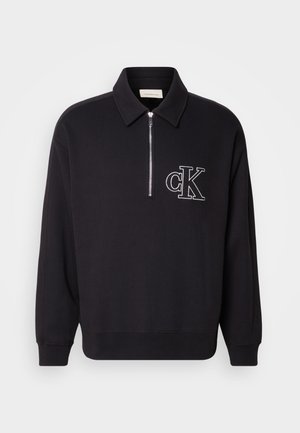 Schwarzer Langarm-Pullover mit Kragen, halb durchgehendem Reißverschluss vorne, gerippten Bündchen und Saum sowie weiß gesticktem "cK" Logo auf der linken Brust.