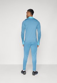 Top y pantalones deportivos de manga larga azul claro, con acentos en azul aqua contrastantes. Confeccionados en un tejido suave, de diseño ajustado y con detalles de costura.