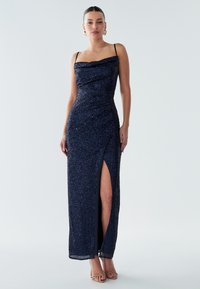 Navy sequin gown with off-the-shoulder neckline, draped detailing, thigh-high slit, and spaghetti straps. Smooth fabric texture and fit.