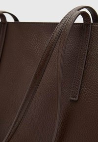 Bruine leren tote bag met een korrelige textuur, voorzien van twee verlengde handvaten en minimale stikseldetails.