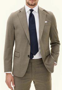 Lichtbruin op maat gemaakt pak met een textuurafwerking, enkelvoudige blazer en gelapte revers. Gekozen met een marineblauwe stropdas en een wit shirt.