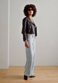 Črna usnjena krajšana jakna s srebrnimi zadrgami, svetlo modri visokotlačni jeans in črne pete s špičastim prstom. Dodatki vključujejo temna sončna očala.