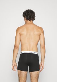 Schwarze Boxershorts mit einem weißen elastischen Bund, der mit "ONLY & SONS" Branding versehen ist. Das Material wirkt glatt und dehnbar. Rückansicht gezeigt.