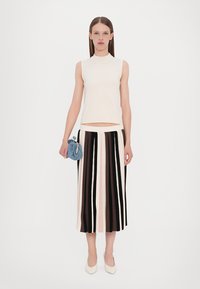 White sleeveless top paired with a striped midi skirt in shades of black, pink, and cream. Accessorized with a small blue bag and white heels.