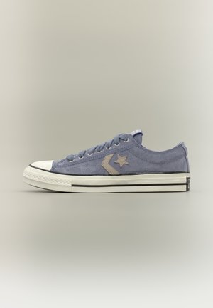 Baskets basses en daim bleu avec embout en caoutchouc blanc, logo étoile et chevron, semelle intermédiaire blanche avec des rayures noires, et fermeture à lacets.