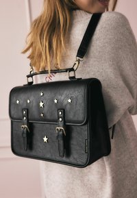 Czarna torebka z ekoskóry z złotymi gwiazdkami, podwójnymi klamrami i regulowanym paskiem. Strukturalny kształt z górnym uchwytem.