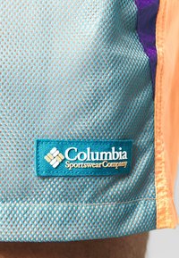 Bleděmodré síťované šortky s oranžovými akcenty, s přišitým štítkem společnosti Columbia Sportswear. Textura je prodyšná s malými perforacemi.