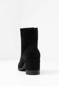 Bottine en suède noire avec un bout arrondi et un talon épais. Texture lisse, design sans coutures et un détail de logo subtil sur le talon.