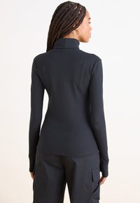 Top preto de manga longa canelado com gola alta, design ajustado e tecido texturizado, combinado com calças cargo pretas.