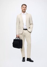 Šviesiai rudos spalvos kostiumas su iškirptėmis atvartais, derinamas su balta marška. Juodi odiniai batai ir struktūrizuota juoda odinė portfelis. Lygi tekstūra.