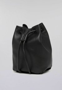Czarna skórzana torba typu bucket o miękkiej fakturze, okrągłej podstawie i zapięciu na sznurek. Na górze znajdują się dwa przelotki na sznurki.