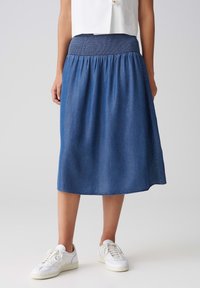 Jeanskjol med smockad midja, knälång, i en mellanblå nyans. Avslappnad passform, parat med vita sneakers.