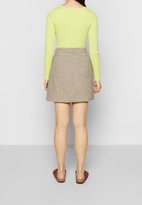 Haut à manches longues vert clair associé à une jupe en tweed marron avec un motif subtil, des poches arrière et une taille ajustée. Sandales plates marron.