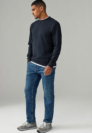 Marineblå crewneck sweatshirt med ribbede manchetter, parret med lyseblå denim jeans og grå sportssko med hvide accenter.