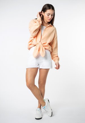 Peach-colored, button-up shirt with a tied front and balloon sleeves, paired with white, scalloped hem shorts and white sneakers.