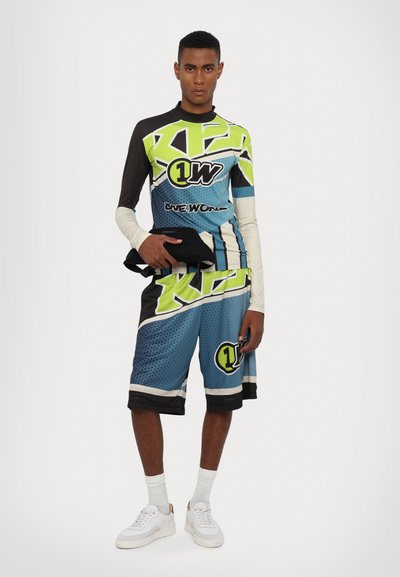 Tenue de sport comprenant un haut à manches longues et un short en bleu, noir et vert fluo, agrémentée de motifs graphiques et d'accents de logo.