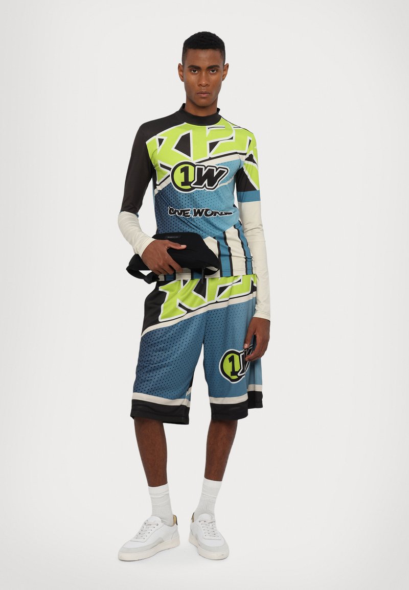 Sportstøj bestående af en langærmet top og shorts i blå, sort og neongrøn, med grafiske mønstre og logo-accenter.