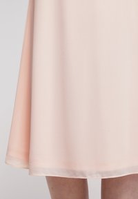 Jupe rose clair en tissu lisse et léger avec une coupe évasée, présentant un léger éclat et un ourlet tombant juste au-dessus du genou.