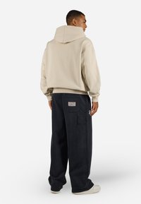 Beige hettegenser med ribbestrikkede mansjetter, kombinert med mørk marineblå cargo-bukser med sidelommer og et merke på baklommen.
