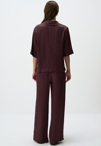Tweerichting outift in donkere stof met een diamantpatroon in rood en roze. De top heeft korte mouwen en een kraag, gecombineerd met wijde broekspijpen.