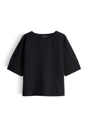 Haut noir à manches courtes en tissu mélange de coton. Présente un col large et une coupe décontractée avec des manches raglan. Texture lisse.