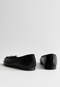 Ballerines en cuir noir avec une texture lisse, un bout arrondi et un accent en nœud en dentelle à l'avant. Semelle basse sans talon.