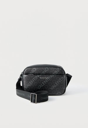 Juoda Valentino per petį nešiojama rankinė su reguliuojama dirželiu, priekinėje dalyje esanti užtrauktuko kišenė ir visame paviršiuje matomas firminis logotipų raštas ant paprasto fono.