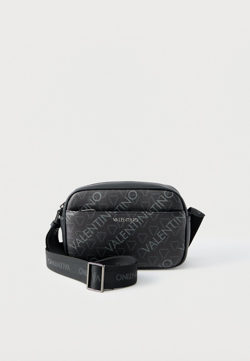 Μαύρη τσάντα Valentino ώμου με ρυθμιζόμενο λουρί, μπροστινή τσέπη με φερμουάρ και ολοκληρωμένο μοτίβο με λογότυπο σε απλό φόντο.