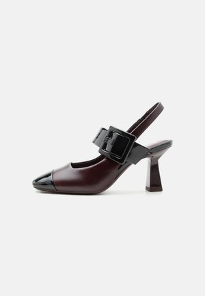 Donkerbruine slingback pump met zwarte lakleren neuskap, stevige middenhoge hak en brede zwarte gespband over de wreef.