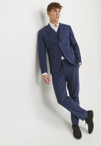 Costum bleumarin dintr-un material texturat, featuring o jachetă cu două butoane și pantaloni asortați. Pantofi negri completează ținuta.