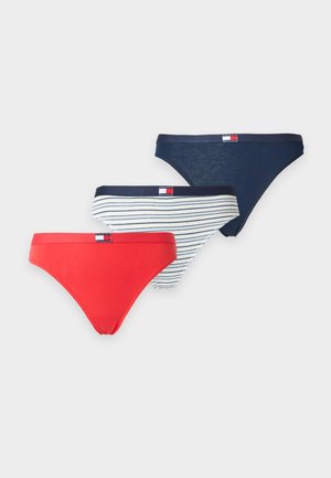 Kvinde står barfodet med den ene hånd på hoften iført en blå og hvid bikini mod en ensfarvet lys baggrund.