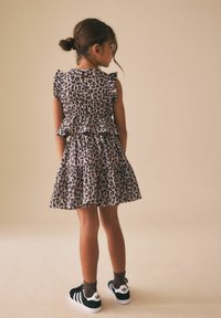 Šaty s leopardím potiskem, volánky, vrstveným designem a detailem zad s průstřihem. Nošeny s černo-bílými teniskami a hnědými ponožkami.