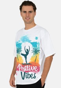 Witte katoenen T-shirt met een kleurrijk grafisch ontwerp met palmbomen, een silhouet van een danser en de tekst "Positive Vibes" in levendige kleuren.