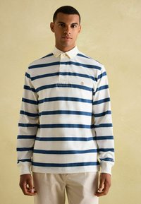 Koszulka rugby z długim rękawem, ozdobiona poziomymi niebieskimi i białymi paskami, z kołnierzykiem i wyszywanym logo na piersi.