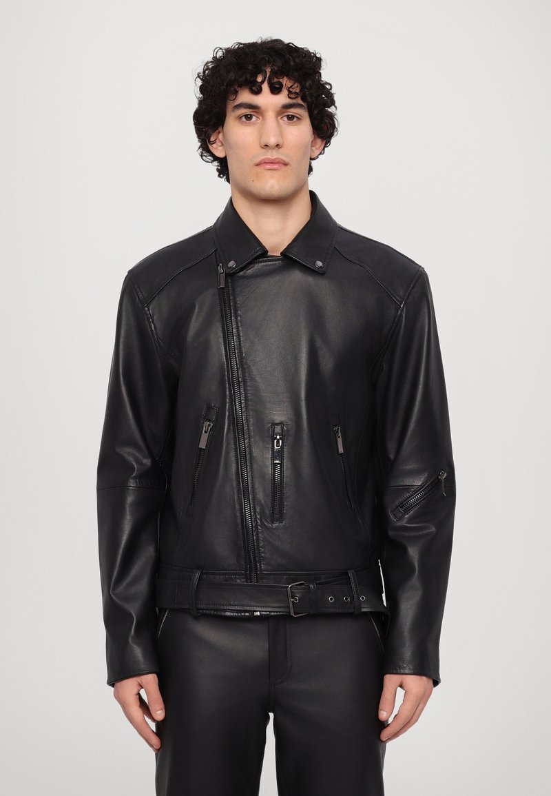 Zwarte leren motorjack met een getailleerd ontwerp, ritsen op de voorkant en mouwen, en een verstelbare taille met riem.
