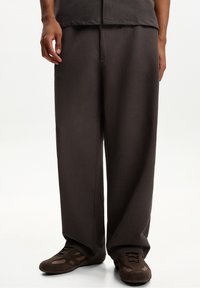 Mörkbruna avslappnade byxor med en strukturerad tygkvalitet, med en rak bendesign och subtila sömdetaljer, kombinerade med bruna sneakers.