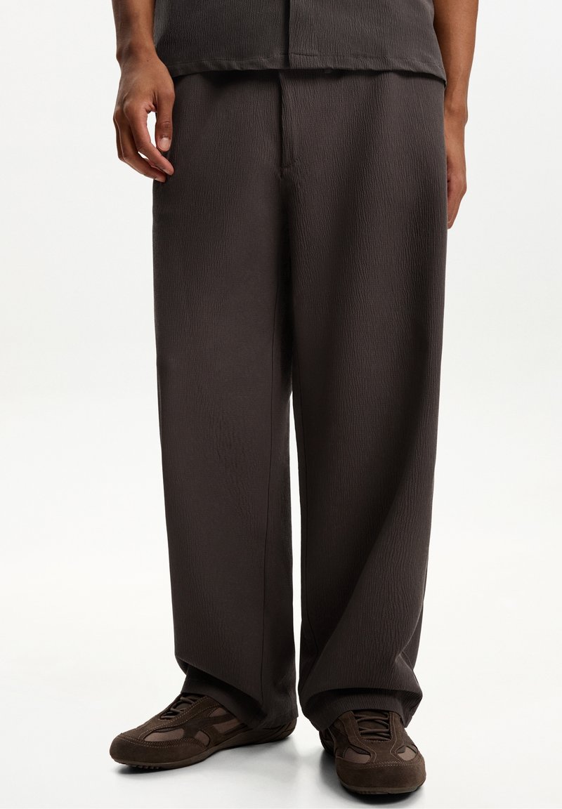 Mörkbruna avslappnade byxor med en strukturerad tygkvalitet, med en rak bendesign och subtila sömdetaljer, kombinerade med bruna sneakers.
