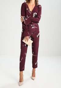 Mono burdeos con estampado floral, de mangas largas acampanadas y escote en V, con una textura suave y una silueta ajustada. Combinado con un bolso de mano ligero.