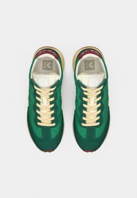 Πράσινα αθλητικά παπούτσια με σουέντ υλικό, κρεμ κορδόνια και μπεζ μεσαία σόλα. Διακριτικές κόκκινες λεπτομέρειες κοντά στη φτέρνα και λογότυπο στην ενδιάμεση σόλα.