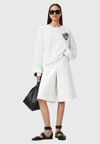 Felpa bianca con grafica nera, pantaloni larghi bianchi, borsa tote nera e sandali piatti neri con cinturini e fibbie.
