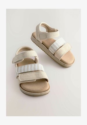Beige Sandalen mit zwei verstellbaren Klettverschlüssen, weichem wildlederähnlichem Material, strukturierten Details und einer geriffelten Gummisohle.