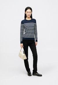 Maglione a righe navy e bianche a maglia con maniche lunghe, abbinato a jeans skinny neri. Porta una borsa beige chiaro e indossa mocassini neri.