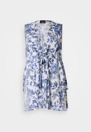 Blomstermønstret vest i hvit med blå blomster, laget av lett stoff. Har V-hals og belte i midjen for justerbar passform.