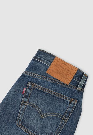 Dunkelblaue Denim-Jeans mit gelben Nähten, ausgestattet mit einem braunen Lederpatch am Bund und einem markanten Design auf der Gesäßtasche.